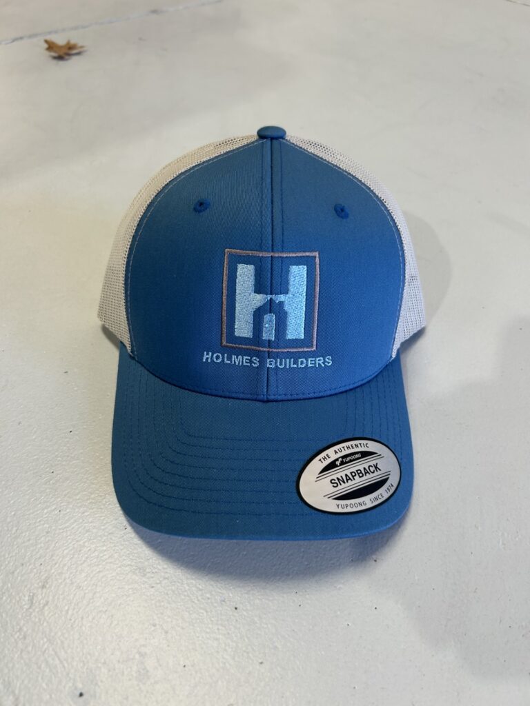 Blue and white Yupoong snapback trucker hat featuring custom embroidered Holmes Builders corporate logo.